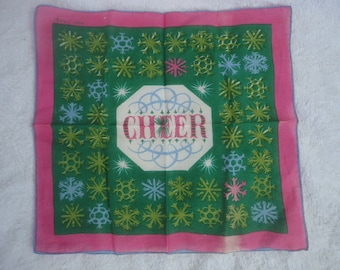 May include: A square fabric handkerchief featuring a dark green center with a repeating pattern of light green, blue, and pink snowflakes. The center contains an octagonal white shape with the word CHEER in red letters.