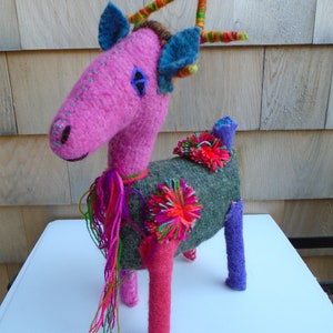 May include: A pink felt deer with blue and green felt accents, a green, pink, and purple yarn tail, and a gray felt body with pink and green felt flowers.