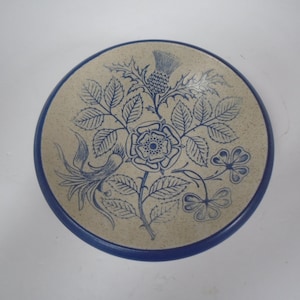 May include: A small, round, ceramic dish with a blue and white floral design. The design features a rose, a thistle, and two butterflies.