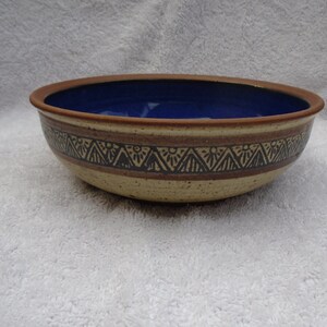 May include: A large, brown ceramic bowl with a blue glaze inside. The bowl has a decorative band of black and brown triangles around the rim.