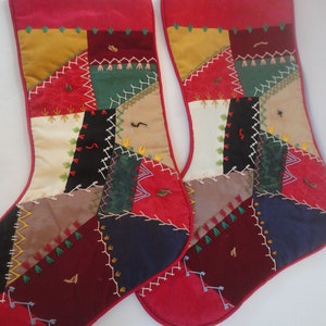 May include: Two Christmas stockings with a patchwork design. The stockings have a red velvet top and bottom, with a variety of colorful fabric patches in between. The patches are stitched together with white thread, and some have embroidered details.