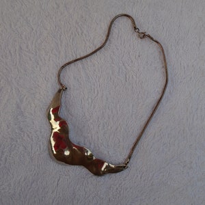 May include: A silver necklace with a wavy, abstract pendant. The pendant is made of a smooth, reflective metal.