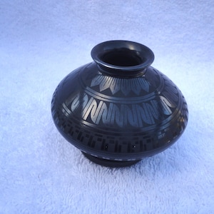 May include: A black ceramic vase with a geometric design. The vase has a round body and a narrow opening.