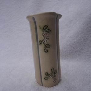 May include: A cream-colored ceramic vase with a floral design. The vase has vertical blue stripes and a floral pattern with green leaves and pink flowers.