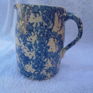 May include: A blue and white ceramic pitcher with a mottled glaze pattern. The pitcher has a wide mouth and a handle.