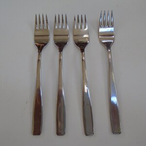 May include: Four silver forks with a simple, modern design. The forks are arranged in a row on a white surface.