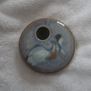 May include: A round ceramic vase with a blue and white glaze. The vase has a small hole in the center for flowers. The vase is decorated with a swirling pattern.