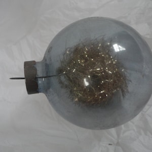 May include: A clear glass Christmas ornament with a gold tinsel filler inside. The ornament has a silver cap and a wire hanger.