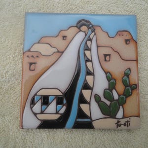 May include: Square ceramic tile featuring a Southwestern desert scene. The design includes a figure in white robes, a blue river, tan mountains, and green cacti. The tile has a glossy finish and is signed in the lower right corner.