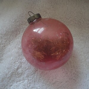 May include: A pink glass Christmas ornament with a silver top and gold glitter inside.