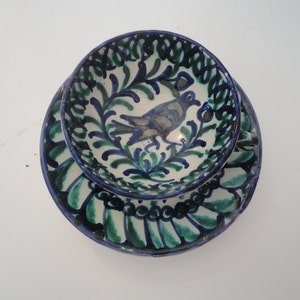 May include: A blue and green ceramic teacup and saucer set with a floral design and a bird in the center.