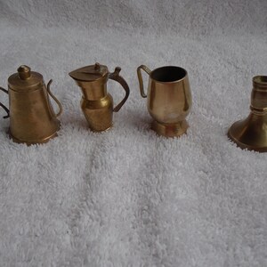 May include: Four miniature brass items: a teapot, a pitcher, a cup, and a candlestick. The items are all made of polished brass and have a traditional design.
