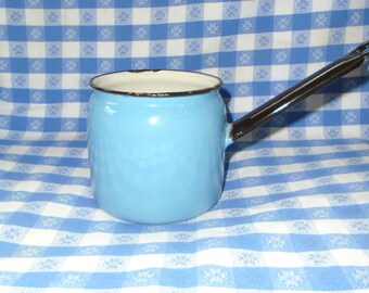 May include: A light blue enamel saucepan with a black handle. The saucepan is on a blue and white checkered tablecloth.