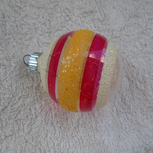 May include: A clear glass Christmas ornament with red and yellow stripes and a glittery finish.