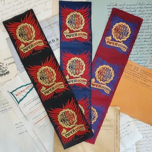 May include: Three rectangular fabric strips featuring a repeating crest design with the text L'IMPER and IMPER OCEANA. The strips are black, blue, and maroon, each displaying a central shield surrounded by red or blue flames and a gold banner.