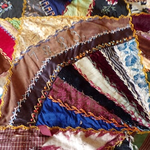 May include: A patchwork quilt featuring various fabric textures including velvet, silk, and patterned cotton in shades of red, blue, brown, and gold. The pieces are joined by decorative yellow embroidery stitches, with the year 1883 embroidered in thread.