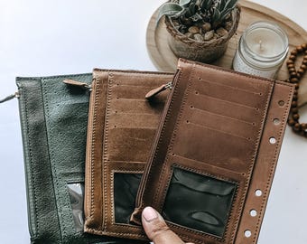 May include: Three leather wallets in shades of green and brown. The wallets have a zippered closure, clear ID windows, and multiple card slots. One wallet is open, revealing the interior design. The wallets are designed for organizing cards and cash.