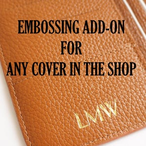 May include: Close-up of a brown leather wallet with the text "EMBOSSING ADD-ON FOR ANY COVER IN THE SHOP". The wallet has a textured surface and gold embossed initials "LMW".