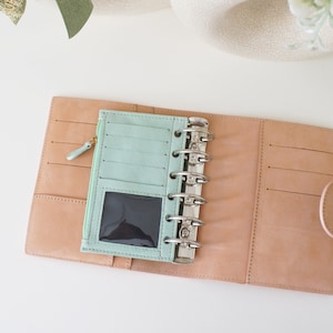 May include: A white ceramic mug with a black handle and the text "But First, Coffee" in a bold, black font. The mug is sitting on a wooden surface. The mug is 4 inches tall.