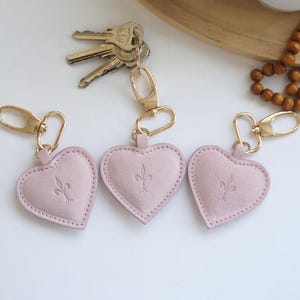 May include: Three pink leather heart-shaped keyrings with gold metal rings and clasps. Each keyring has a different floral design embossed on the front.