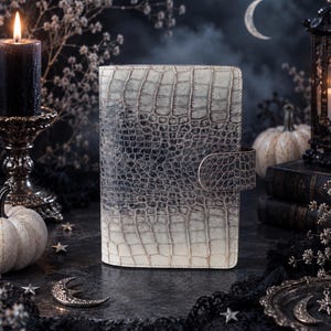 May include: A rectangular notebook cover featuring a textured, embossed crocodile skin pattern that transitions from a dark charcoal gray at the top to a light cream color at the bottom, complete with a matching side closure strap.
