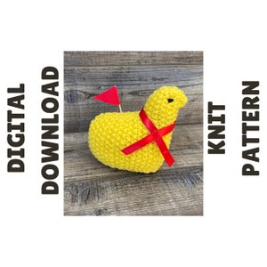 May include: Knit pattern for a yellow chick with a red ribbon and a red flag. The chick is sitting on a wooden surface.