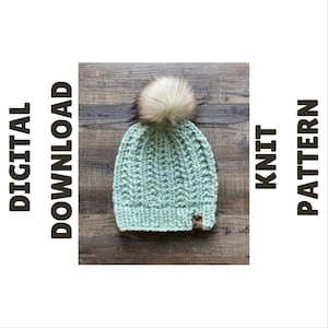 Puede incluir: Un gorro de punto verde claro con un pompón de piel sintética. El gorro tiene una textura acanalada y una pequeña etiqueta marrón. Las palabras "DESCARGA DIGITAL" y "PATRÓN DE PUNTO" están impresas verticalmente en los lados.