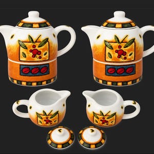 May include: Two ceramic teapots with lids, two matching creamers, and two separate lids. The white ceramic features a hand-painted design of orange and yellow gradients, green leaves, red berries, and a blue rectangular band with red coffee beans.