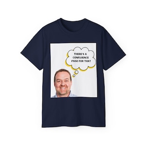 May include: A navy blue short-sleeve t-shirt featuring a square graphic on the chest. The graphic displays a smiling person and a white thought bubble with a yellow outline containing the black text, THERE'S A CONFLUENCE PAGE FOR THAT.