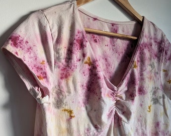May include: A pink, yellow and grey tie-dye t-shirt with a v-neck and short sleeves. The shirt is hanging on a wooden hanger.