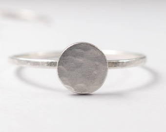 May include: A silver ring with a hammered, oval-shaped top. The ring is thin and delicate.