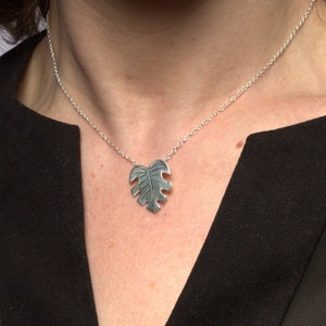 May include: A silver necklace with a leaf-shaped pendant. The pendant is detailed with a textured design.