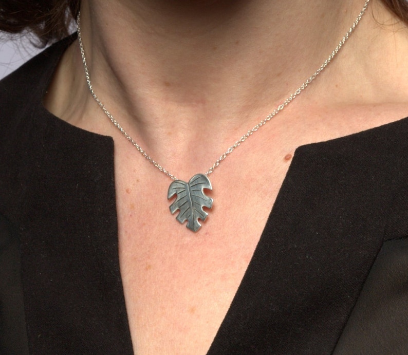 May include: A silver necklace with a leaf-shaped pendant. The pendant is detailed with a textured design.