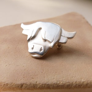 May include: A silver Highland cow brooch, a traditional Scottish symbol, with a detailed design and a brushed finish.
