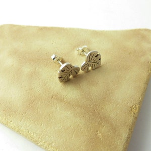 May include: A pair of silver stud earrings featuring a leaf design. The earrings are small and delicate, and they would make a great gift for someone who loves nature.