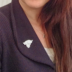 May include: A white cow head pin on a person's dark blue jacket. The pin is a simple silhouette of a cow's head.