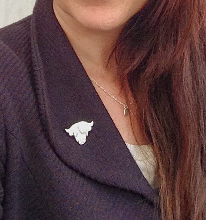 May include: A white cow head pin on a person's dark blue jacket. The pin is a simple silhouette of a cow's head.