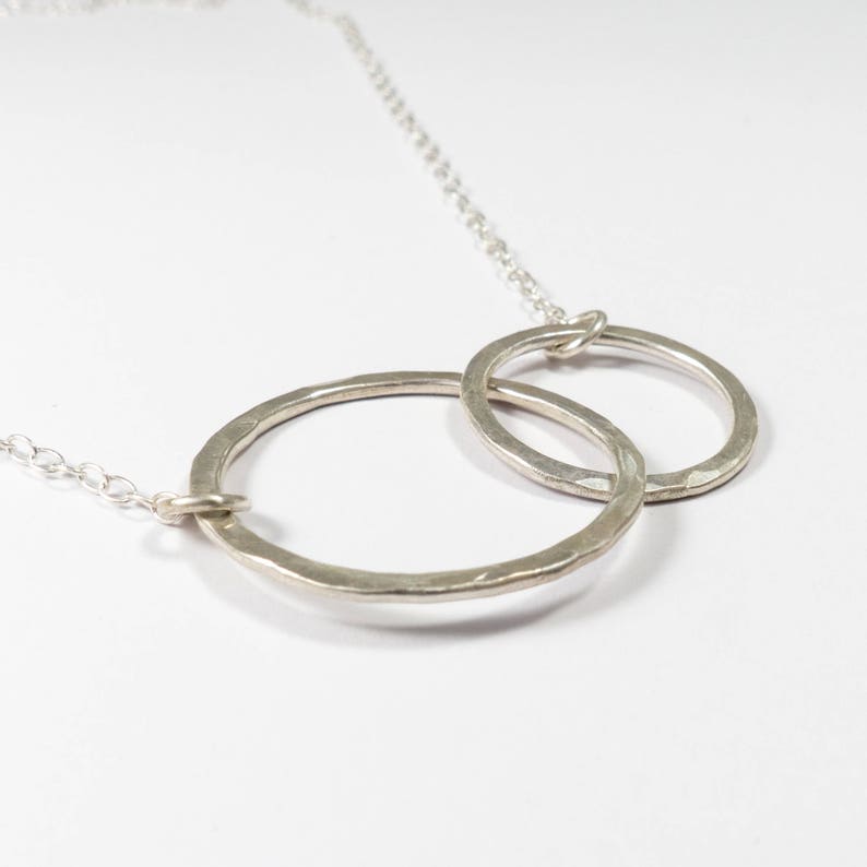 May include: A silver necklace with two interlocking circles. The circles are hammered and have a textured finish.