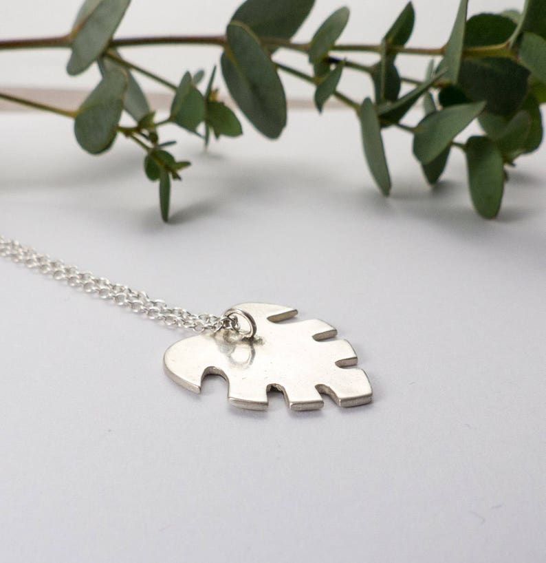 May include: A silver necklace with a delicate chain and a pendant shaped like a monstera leaf.