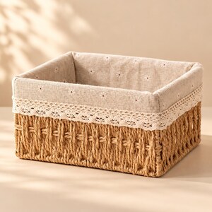 May include: A rectangular storage basket with a woven tan exterior and a beige fabric liner. The liner features a small white floral pattern and is trimmed with a decorative white lace border along the top edge of the basket.