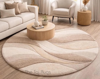 Tappeto rotondo beige, in lana fatto a mano, con motivo astratto a onde, ideale per un soggiorno moderno e neutro.