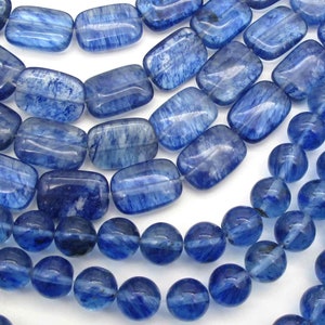 May include: A strand of blue kyanite gemstone beads, featuring both round and rectangular shapes. The beads have a translucent, slightly cloudy appearance with a light blue color.