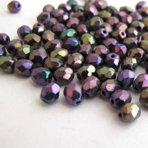 May include: A pile of iridescent purple and green glass beads. The beads are faceted and have a metallic sheen.