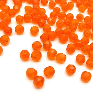 May include: A scattering of small, faceted, orange glass beads on a white background.
