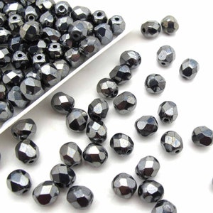 May include: A pile of dark gray faceted glass beads. The beads are scattered on a white surface.