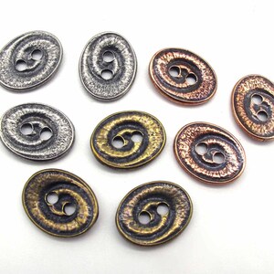 May include: Assortment of oval-shaped metal buttons with a swirl design. The buttons are in silver, copper, and brass tones.