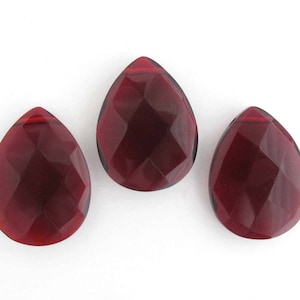 May include: Three faceted teardrop-shaped glass beads in a deep red color.