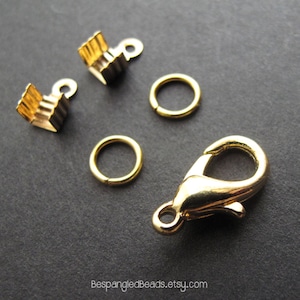 May include: Gold-toned jewelry making supplies including two crimp beads, two jump rings, a lobster clasp, and a small round ring.