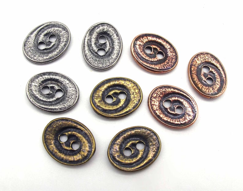 May include: Assortment of oval-shaped metal buttons with a swirl design. The buttons are in silver, copper, and brass tones.
