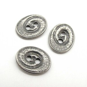 May include: Three silver oval-shaped buttons with a textured surface and two holes each.